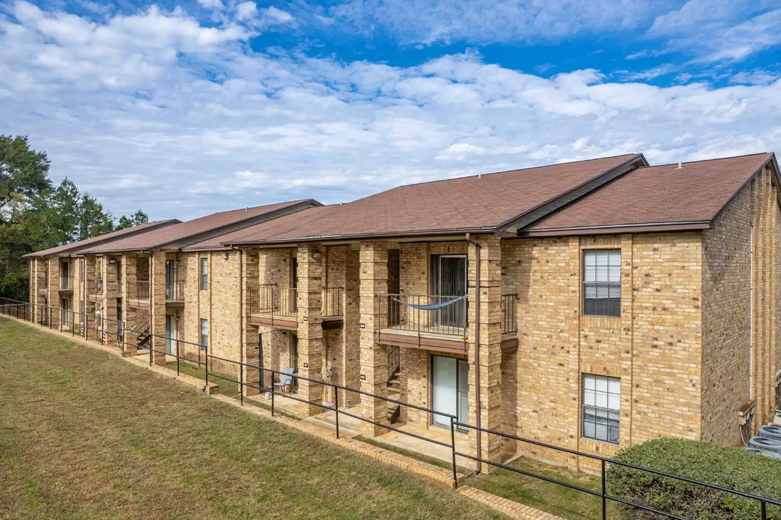 Exterior view of brick apartment building with balconies and sloped roof.