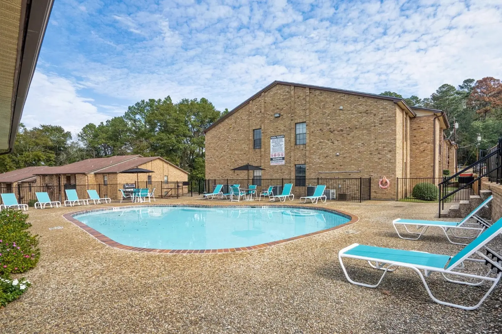 Outdoor pool area with lounge chairs at brick apartment complex.