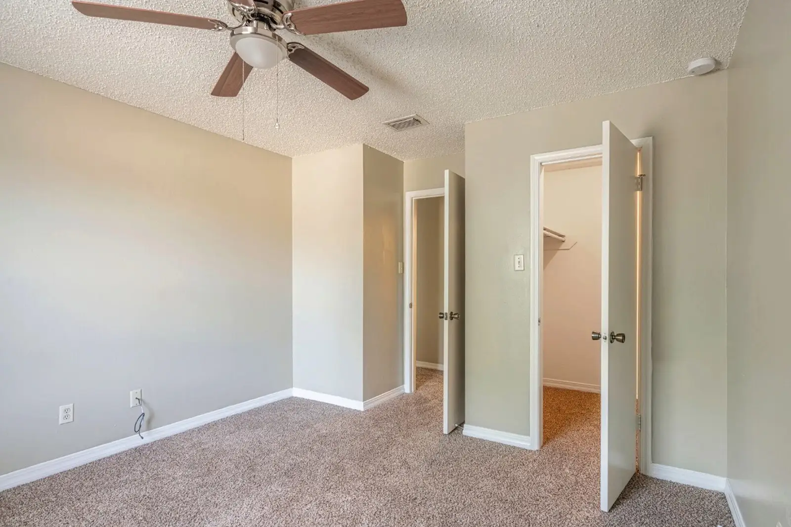 Carpeted bedroom with ceiling fan and open closet doors.