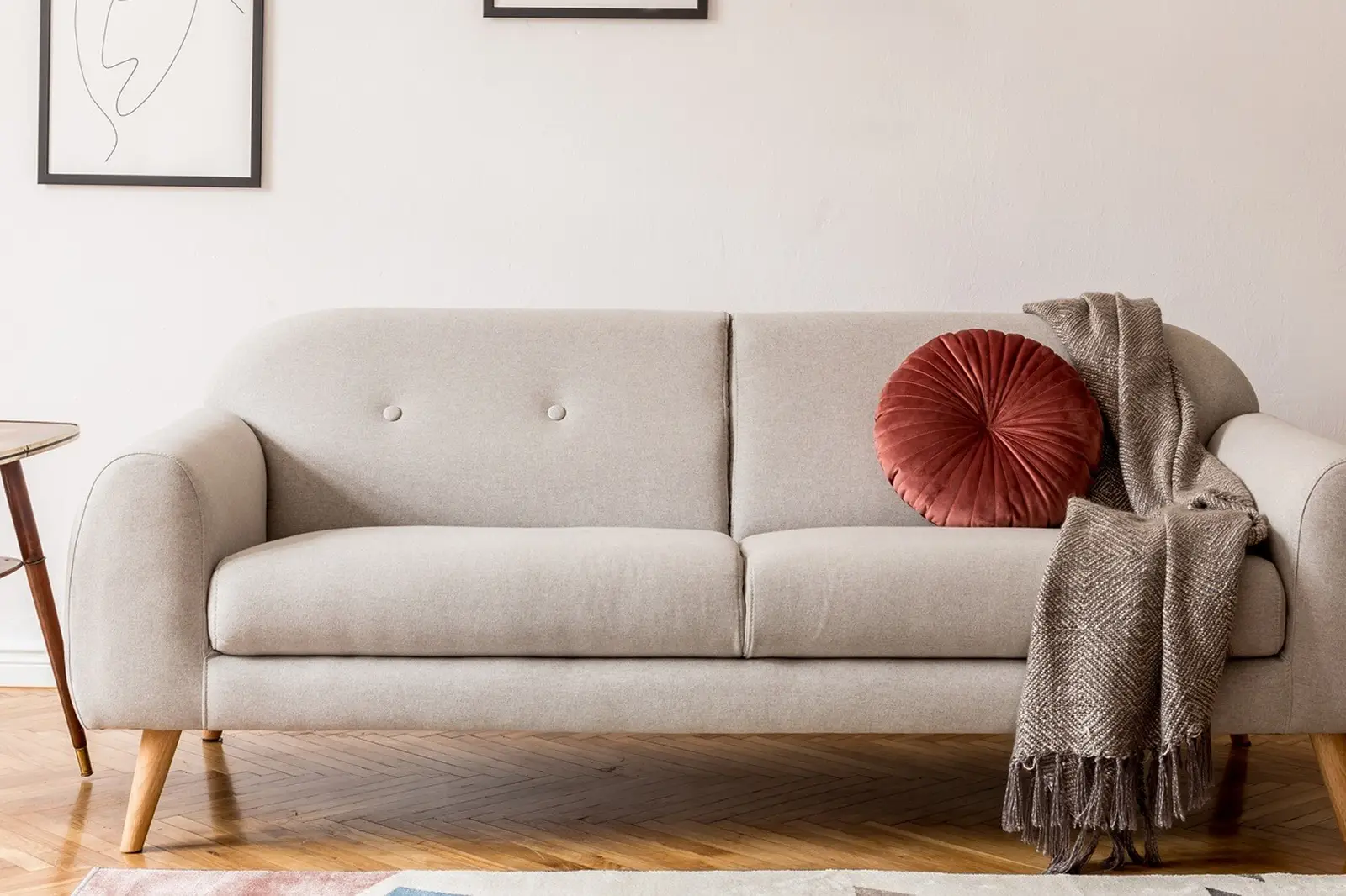 Modern beige sofa with round pillow and throw blanket.