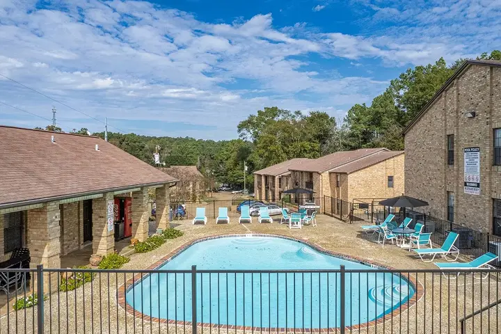 Fenced swimming pool surrounded by lounge chairs and brick apartment buildings.