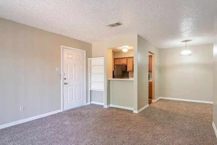 Empty living room with carpet flooring and view of kitchen area.