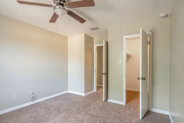 Carpeted bedroom with ceiling fan and open closet doors.