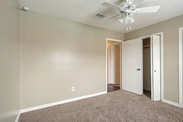 Empty carpeted bedroom with white ceiling fan and closet.